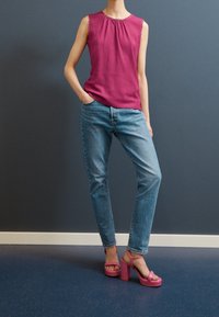 Fuchsia sleeveless top with textured fabric, paired with light blue jeans. Pink high-heeled sandals with a chunky heel and ankle strap.