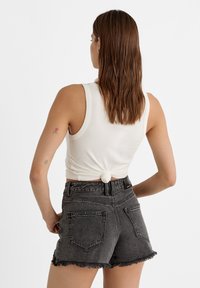 Top corto blanco de canalé anudado en la parte trasera, combinado con pantalones cortos de mezclilla negra de tiro alto con un dobladillo deshilachado y dos bolsillos traseros.