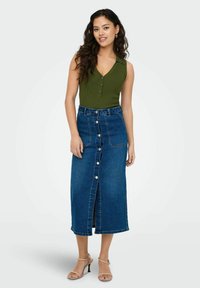 Top senza maniche a coste verde scuro con scollatura a V, abbinato a una gonna di jeans di lunghezza media con bottoni frontali e tasche. Sfondo chiaro.