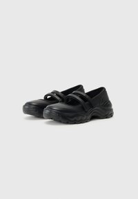 Zapatos casuales negros que presentan un material sintético suave, forma redondeada, suela de goma gruesa y un diseño de doble correa en la parte superior.