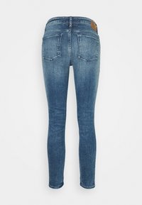 Jeans de denim azul ajustados con un acabado desgastado, dos bolsillos traseros y un parche de cuero marrón en la cintura. Costuras en los tobillos.