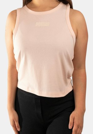 Donna che indossa un top corto senza maniche in costa di colore rosa chiaro abbinato a pantaloni neri, in piedi davanti a uno sfondo chiaro uniforme.