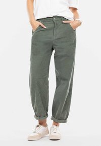 Lässige grüne Cordhosen mit hohem Bund, Fronttaschen und umgeschlagenen Säumen, kombiniert mit weißen Sneakers. Texturiertes Material, lässiges Design.