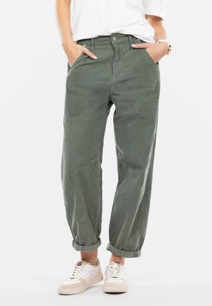 Pantaloni in velluto a coste verde, a vestibilità ampia e vita alta, con tasche frontali e orli arrotolati, abbinati a scarpe da ginnastica bianche. Tessuto testurizzato, design casual.