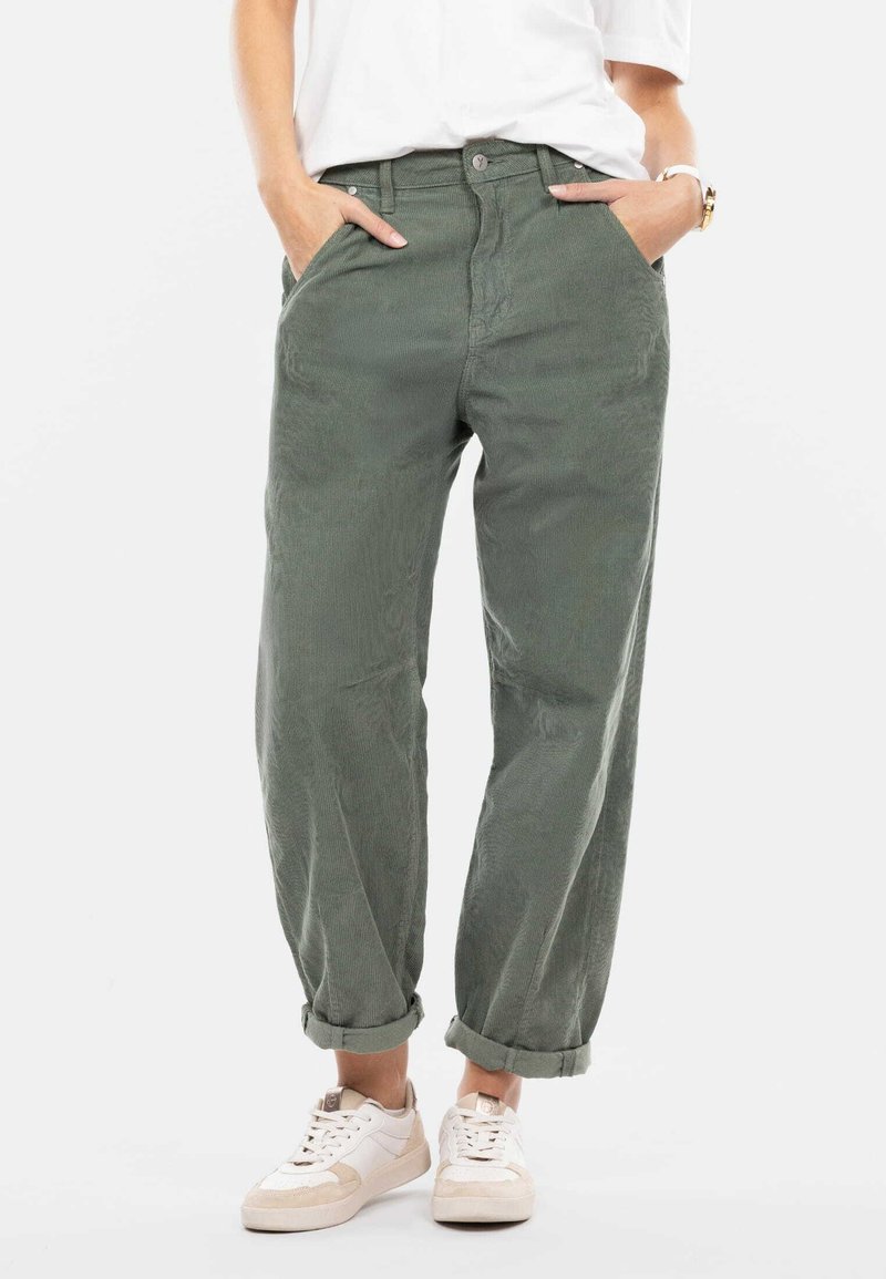 Lässige grüne Cordhosen mit hohem Bund, Fronttaschen und umgeschlagenen Säumen, kombiniert mit weißen Sneakers. Texturiertes Material, lässiges Design.