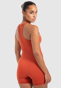 Rostfärgad atletisk bodysuit med racerback-design och korta ben, tillverkad av elastiskt material, med en diskret logotyp nära midjan.