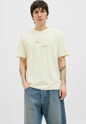 Lys gul bomulds T-shirt med en løs pasform, der har et diskret grafisk print med teksten "Originals Creative Department", parret med blå denim shorts.