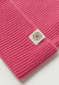 Rosa ribbat tyg med en vikt kant, prytt med en liten krämfärgad etikett med en brun dekorativ logotyp. Den mjuka texturen är synlig.