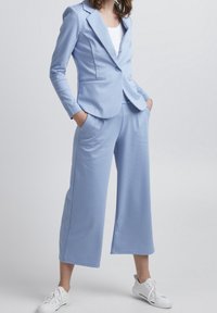 Ljust blå tvådelad outfit med en skräddarsydd blazer och vida byxor, som har en slät textur och avslappnad passform, ihop med vita sneakers.