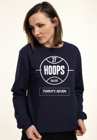 Felpa blu navy con grafica di un pallone da basket rotondo e testo "27 HOOPS BALLERS". Include etichetta "TWENTY.SEVEN BASKETBALL".