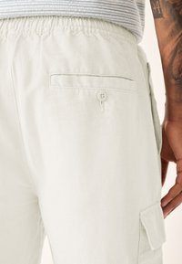 Light-colored cargo shorts made from soft fabric, featuring an elastic waistband, back pocket with button, and side cargo pocket.