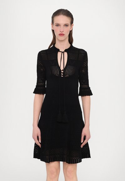 Vestito nero lavorato a maglia con collo alto, maniche corte con bordi svasati, e un design con aperture e frange in vita.