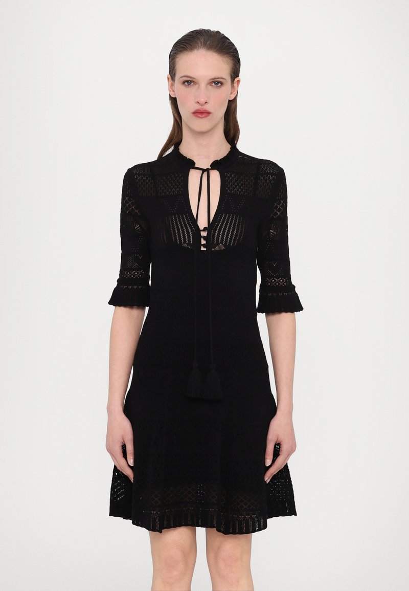 Schwarzes gestricktes Kleid mit hohem Hals, kurzen Ärmeln mit ausgestellten Kanten und einem Ausschnitt-Design mit Quastenakzenten an der Taille.