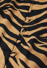 Beige Stoff mit auffälligen schwarzen Zebra-Streifen, mit runden Knopf-Details entlang der Mitte. Die Textur wirkt glatt und leicht matt.