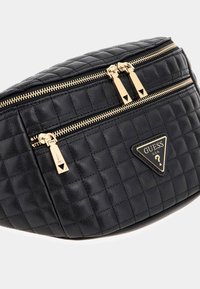 Borsa in vita nera in pelle trapuntata con cerniere dorate ed emblema triangolare del logo Guess sulla tasca anteriore.