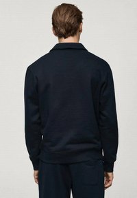 Námořnická mikina s uvolněným střihem, vyrobená z texturované látky. Má límec a žebrované manžety, s viditelnou boční kapsou.