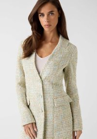 Lichte tweedblazer in pasteltinten met een gestructureerde afwerking, getailleerde pasvorm, kragen met inkeping, twee knopen en een zijzakdetail.