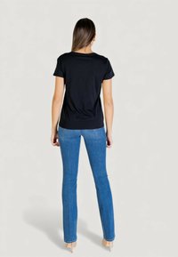 Czarny t-shirt z krótkim rękawem w połączeniu z dopasowanymi niebieskimi dżinsami. Koszulka ma prosty design i gładką fakturę. Modelka ma na sobie beżowe szpilki.