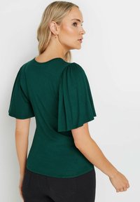 Top verde oscuro con mangas cortas abullonadas. Textura suave y escote redondo. Silueta ajustada con un dobladillo curvado en la parte posterior.