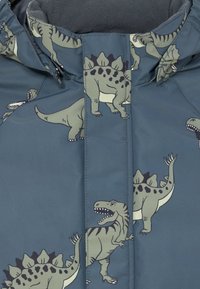 Giacca imbottita blu con illustrazioni di dinosauri verdi e neri, con disegni di T-Rex e Stegosauro sul tessuto.