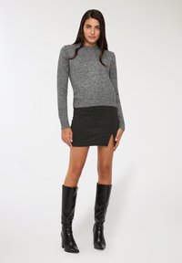 Maglione grigio a maglia, mini gonna nera a righe con uno spacco laterale e stivaletti neri con tacco al ginocchio; trame morbide e design attillato.