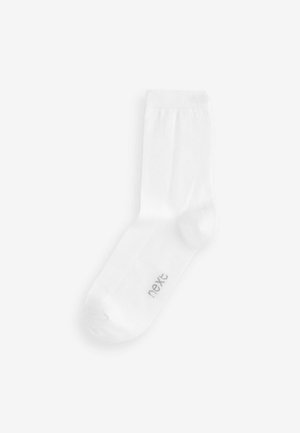 Chaussette en coton blanc avec une bordure côtelée, un bout arrondi et un petit logo gris sur le côté. Design simple, texture douce et longueur cheville.