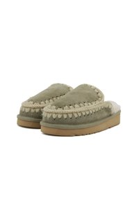 Pantofole in suede verde con rifiniture beige e fodera in shearling. Presentano cuciture dettagliate e una suola piatta in gomma testurizzata.