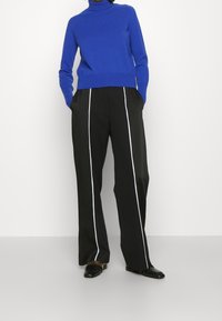 En ljusblå polotröja, figursydd i midjan, tillsammans med svarta byxor med vita sidjoner och platta svarta skor.