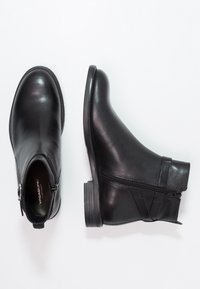 Botas de tobillo de cuero negro con punta redondeada, cremallera lateral y acentos texturizados, presentan un tacón bajo apilado y una superficie lisa.