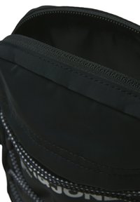 Zwarte nylon rugzak met een ritsvak, met zichtbare witte branding en contrasterende stiksels langs de randen.
