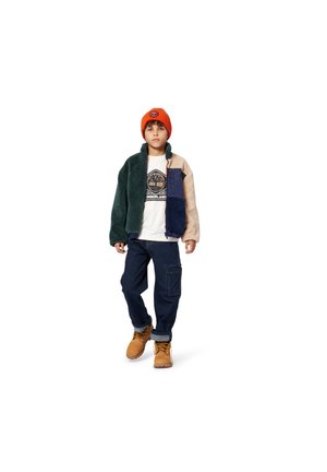 Multi-kleurige fleece jack met donkere groene, beige en marineblauwe panelen, gedragen over een wit t-shirt. Blauwe denim broek en bruine laarzen maken de outfit compleet.