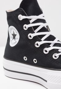 Czarne wysokie sneakersy na płaskiej podeszwie z białymi sznurowadłami, srebrnymi oczkami i gumową podeszwą, z teksturowanym noskiem oraz okrągłą łatą z logo.