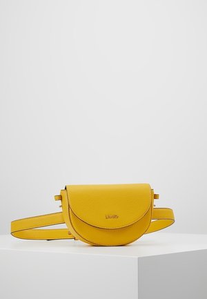 Žlutá texturovaná kožená polokruhová kabelka na opasek s klopou a tenkým nastavitelným popruhem vystavená na bílém podstavci.