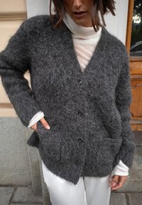 Pilkas, pūkuotas kardiganas su V formos iškirpte, mygtukų uždarymu ir priekinėmis kišenėmis. Dėvimas ant šviesaus turtleneko ir derinamas su baltais kelnėmis.