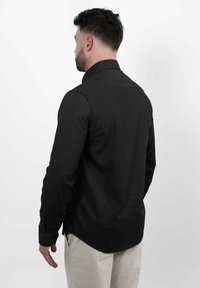 Donker geknoopte shirt met lange mouwen, gemaakt van gestructureerde stof, met een klassieke kraag en een afgeronde zoom. Gemaakt in combinatie met beige broeken.