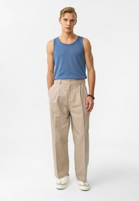 Blauwe mouwloze tanktop met een ronde hals, gecombineerd met beige geplooide broek en witte sneakers met grijze accenten.