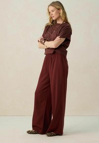 Ensemble deux pièces bordeaux composé d'un haut court à manches courtes et d'un pantalon large. Le tissu semble lisse avec une taille élastique.