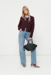 Cardigan bordeaux avec boutons, chemise col bleu clair, jeans bleu clair déchirés, sac à main noir et chaussures à talons grises.