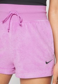 Rosa fleeceshorts med bred elastisk midja och dragsko. Har en svart Nike-logotyp på den nedre fållen för extra detaljer.