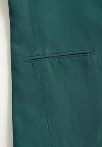 Tessuto turchese con texture liscia; presenta una tasca welt piatta e cuciture pulite, evidenziando un design minimalista e una forma strutturata.