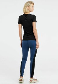 Čierna tričko s krátkym rukávom a textúrovanou panely, spárované s modrými legínami so čiernymi bočnými panelmi. Ľahká, športová silueta, voľnočasový štýl.