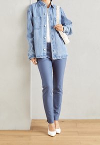 Džínová bunda s přední náprsní kapsou, bílé knoflíky, dlouhé rukávy. Světle modré úzké kalhoty a bílé lodičky s špičatou špičkou dokončují úbor.