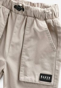 Beige Cargo-Shorts mit elastischem Bund, schwarzem Kordelzug und Fronttaschen. Sie weisen eine Stoffstruktur mit einem kleinen Markenetikett auf.