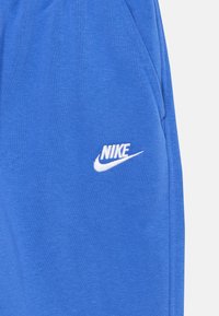Mėlynos sportinės kelnės, pagamintos iš minkštos medvilnės mišinio, su balta Nike logotipo siuvinėjimu kairėje kojoje. Lygus paviršius su elastingu juosmeniu.