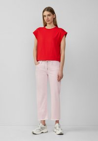 T-shirt rossa in cotone a maniche corte, abbinata a jeans dritti rosa chiaro con orlo sfilacciato, completati da sneaker sportive grigie.
