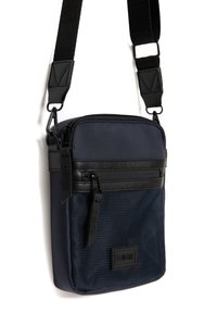 Námořnickomodrá crossbody taška s texturovaným síťovaným předním dílem, černými akcenty, horním zipem a nastavitelným popruhem. Obsahuje logo značky na nášivce.