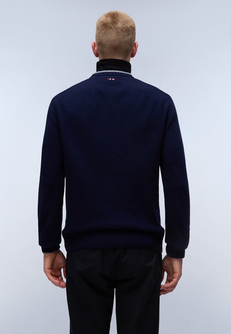 Granatowy sweter z wysokim kołnierzem, prążkowanymi mankietami i dołem. Posiada małe logo na karku. Gładka tekstura i luźny krój.