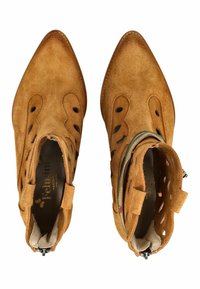 Par de botines marrón claro de ante con punteras puntiagudas, recortes decorativos, cremalleras laterales y un forro interior acolchado de color beige.