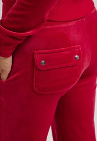 Rode velours broek met een achterzak met drukknoopjes, een gladde textuur, een getailleerd ontwerp en een elastische tailleband.