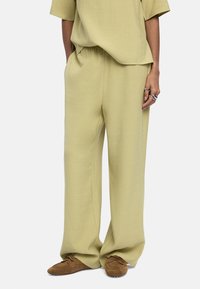 Jasnozielone, luźne spodnie wykonane z miękkiego materiału, z elastycznym paskiem w talii, w połączeniu z brązowymi butami wsuwanymi.
